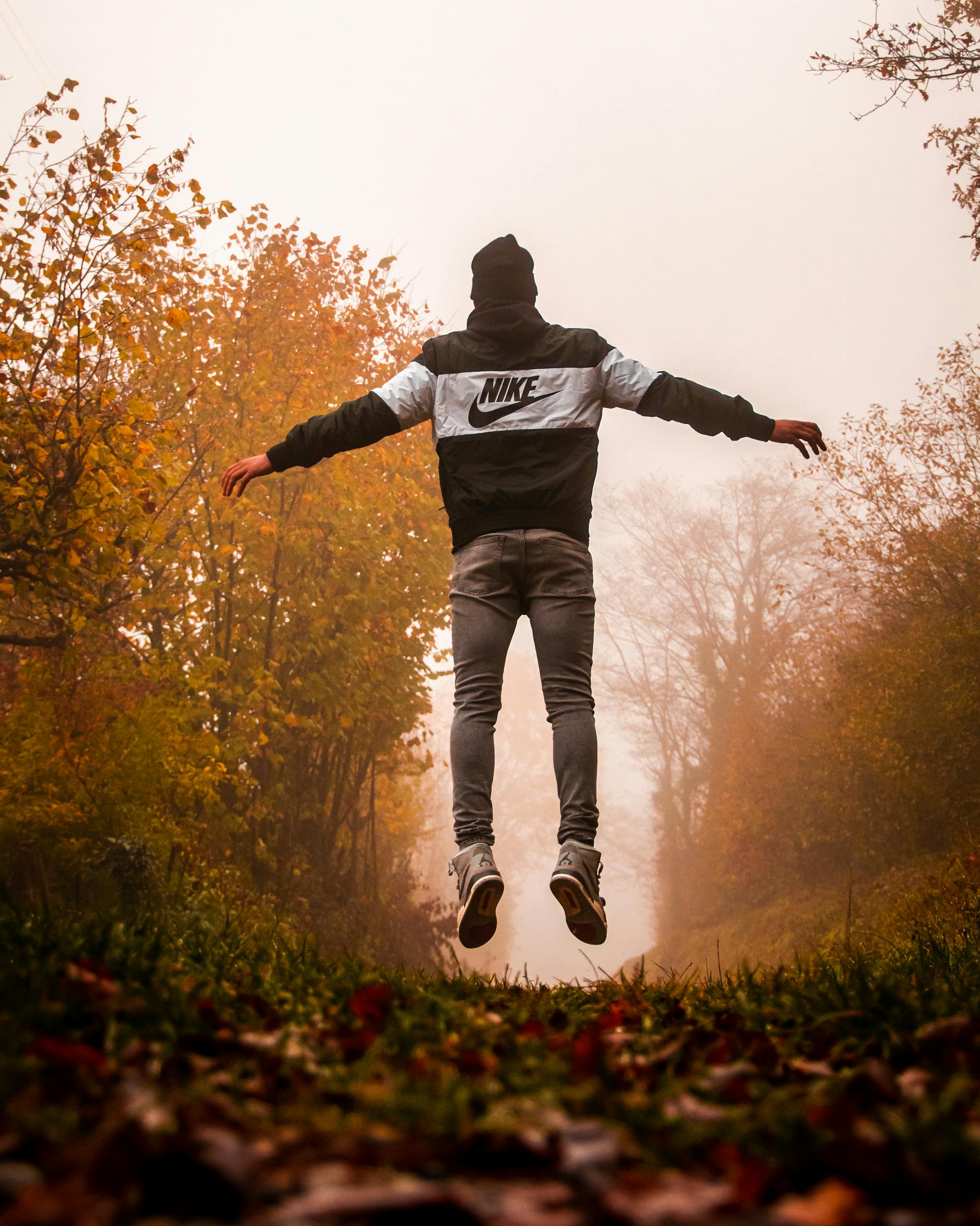 Home A young man in casual wear jumps joyfully on a foggy autumn day in a forest, capturing the essence of nature and freedom.
